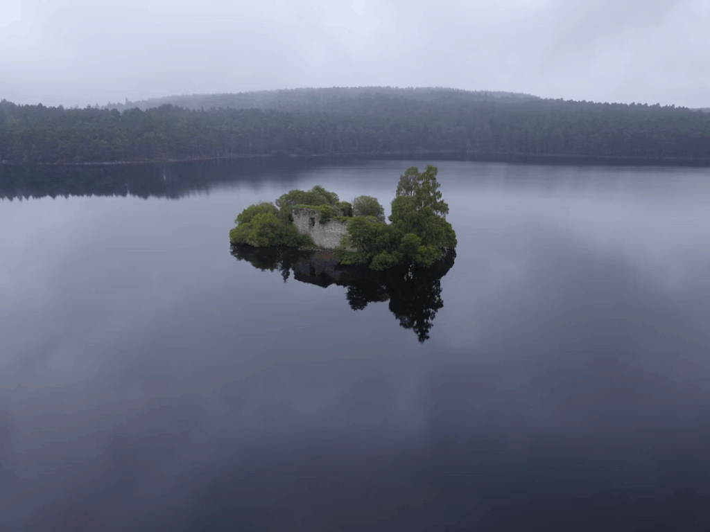 Loch an Eilein, a hidden Scottish loch surrounded by forest, with crystal-clear water reflecting the sky and nearby mountains