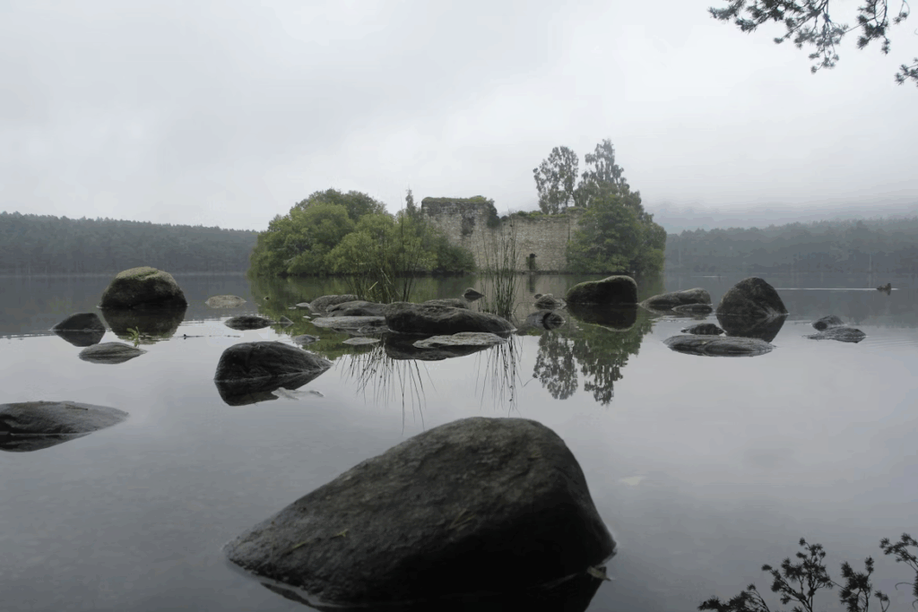 Loch an Eilein, a hidden Scottish loch surrounded by forest, with crystal-clear water reflecting the sky and nearby mountains
