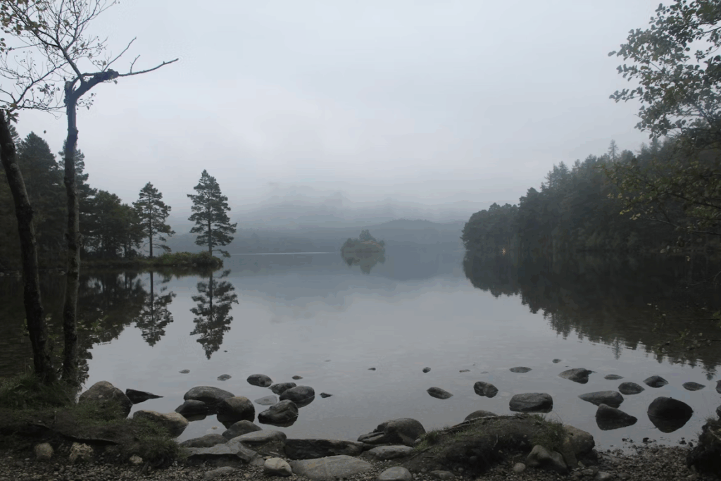 Loch an Eilein, a hidden Scottish loch surrounded by forest, with crystal-clear water reflecting the sky and nearby mountains