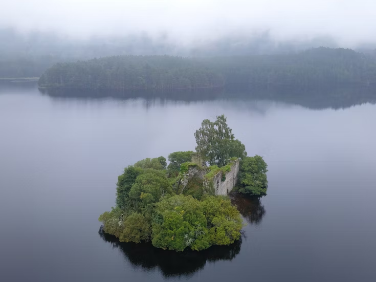 Loch an Eilein, a hidden Scottish loch surrounded by forest, with crystal-clear water reflecting the sky and nearby mountains