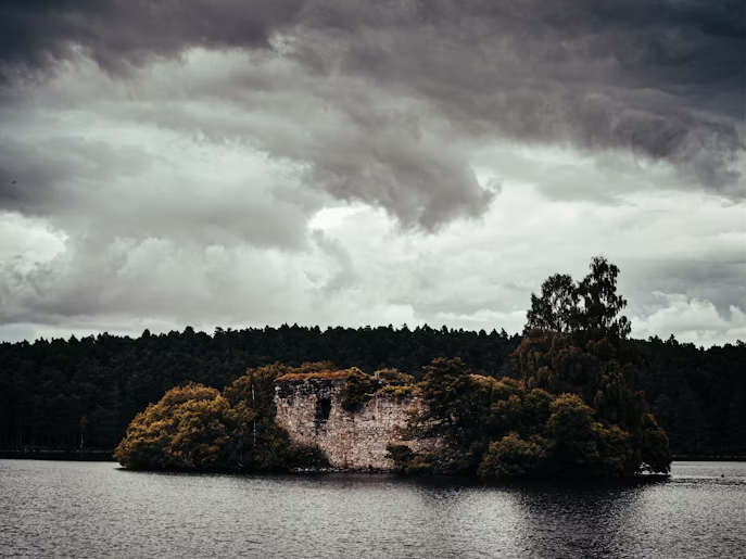 Loch an Eilein, a hidden Scottish loch surrounded by forest, with crystal-clear water reflecting the sky and nearby mountains