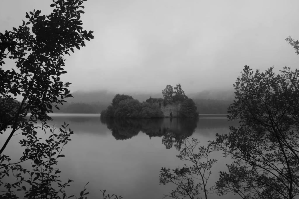 Loch an Eilein, a hidden Scottish loch surrounded by forest, with crystal-clear water reflecting the sky and nearby mountains