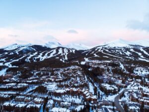 Snowy Breckenridge panorama. A high-angle view captures the town nestled in snow, with rooftops dusted in white and the surrounding mountains blanketed in snow under the morning light.