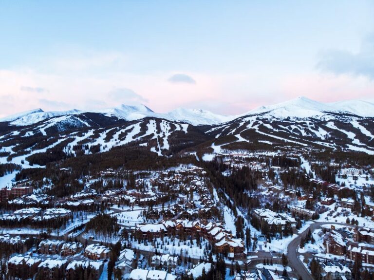 Snowy Breckenridge panorama. A high-angle view captures the town nestled in snow, with rooftops dusted in white and the surrounding mountains blanketed in snow under the morning light.